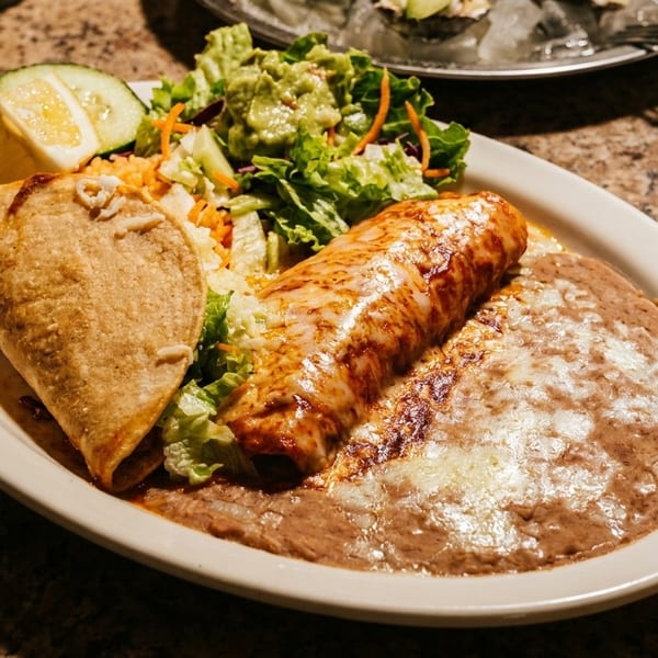 A plate of Mexican food with a taco, enchilada, refried beans, and a side salad.