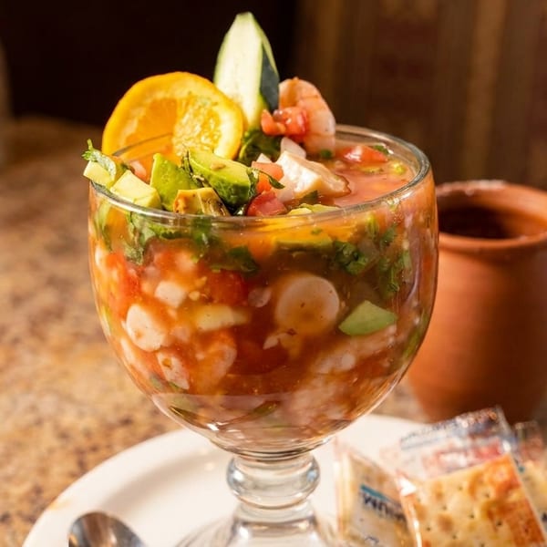 Shrimp cocktail in a goblet with avocado, orange, and cucumber, served with crackers.