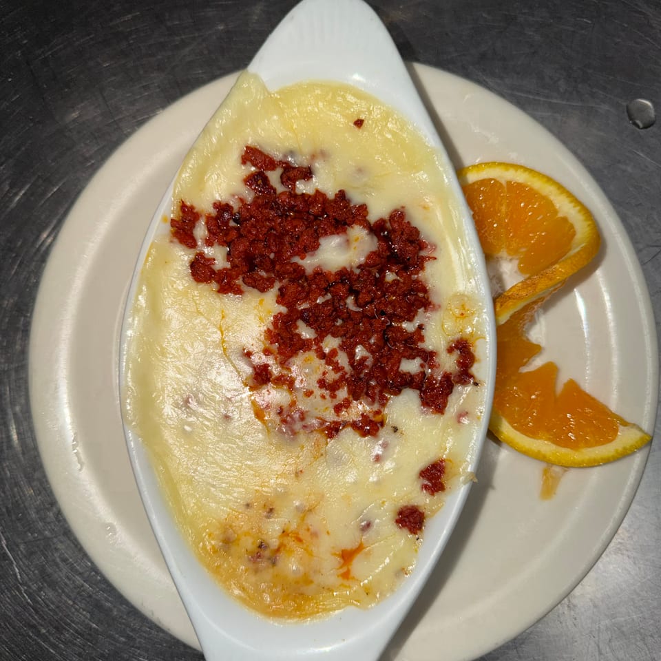 Baked cheesy dish topped with crumbled sausage, served in a white ceramic dish with orange slices.